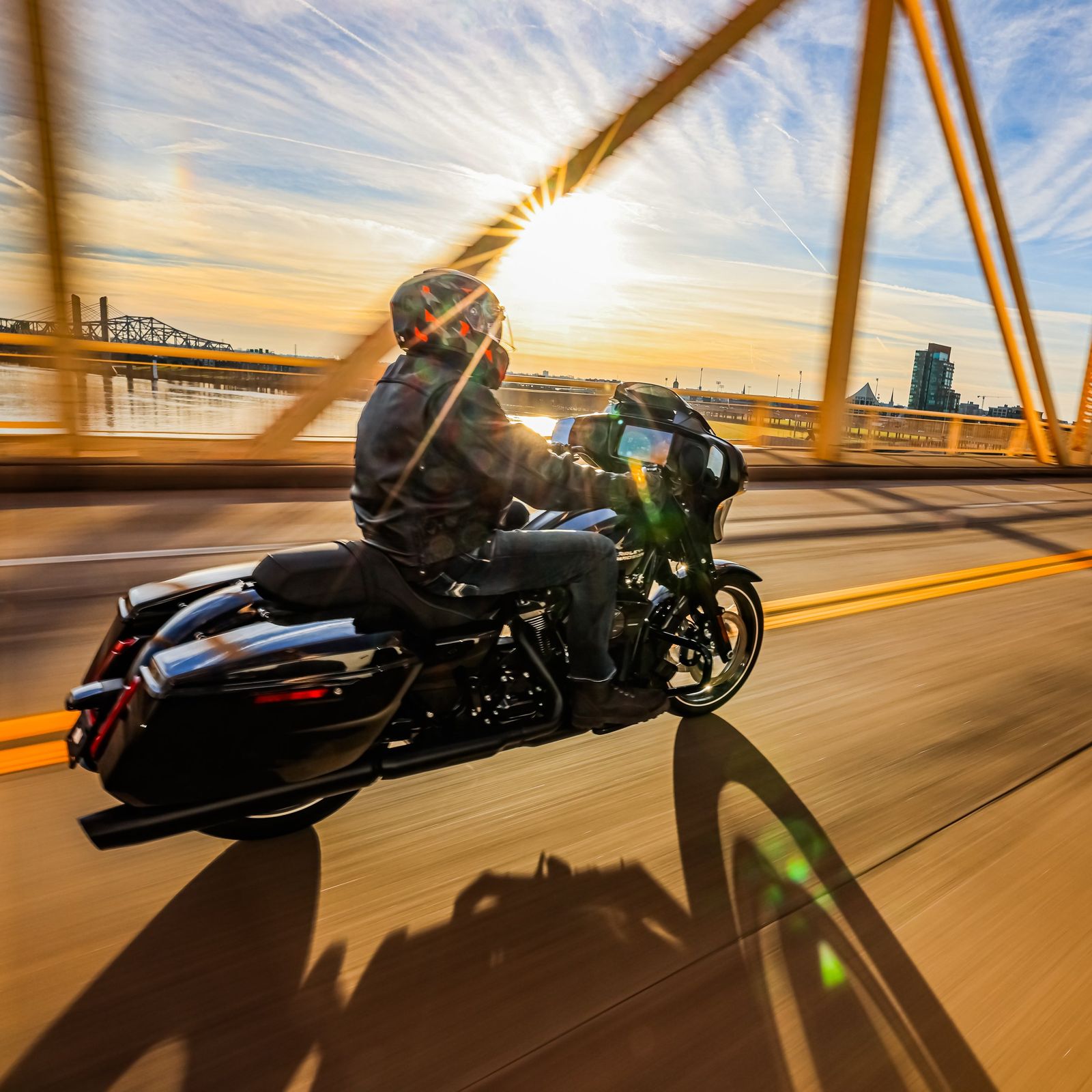 A motorcyclist riding on a highway at sunset with city buildings in the backgrou