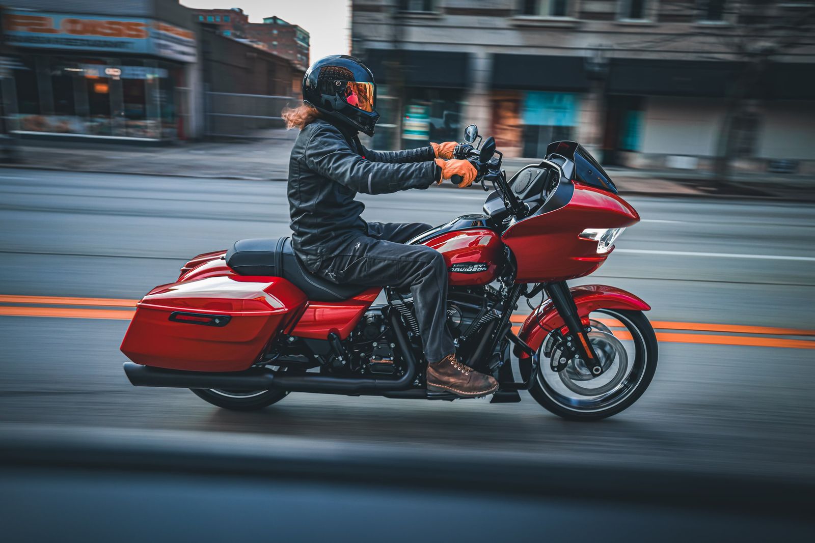 Person riding a red Harley-Davidson touring motorcycle on a city street in motio