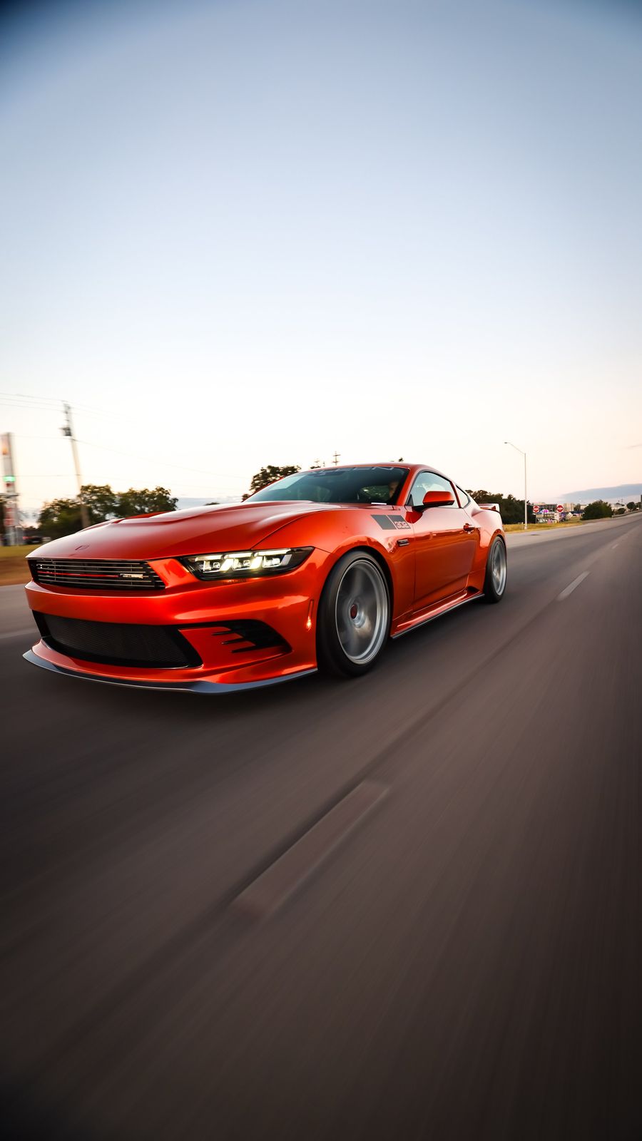Red sports car driving on a highway at sunset.