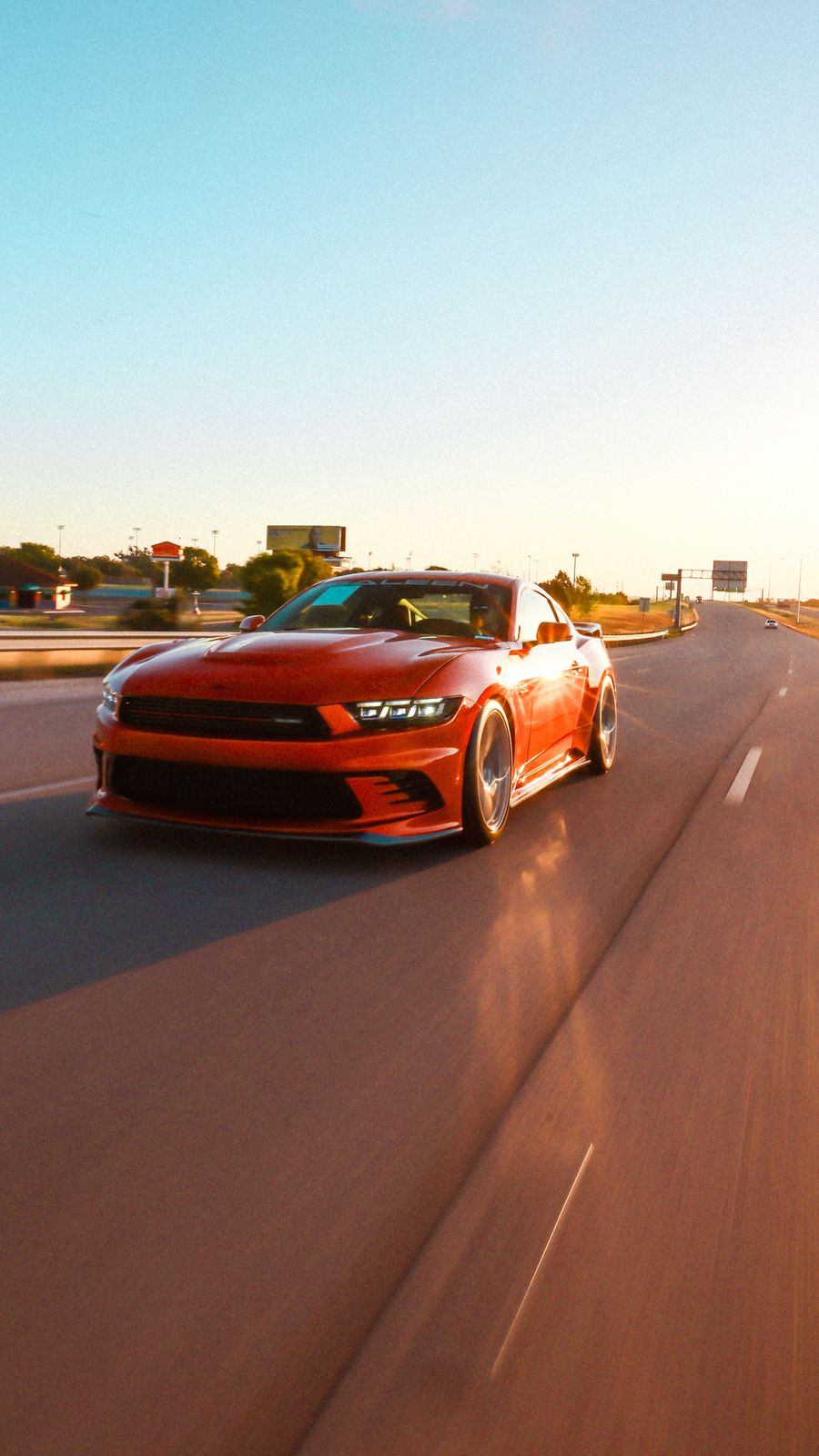 A red sports car driving on a highway during sunset.
