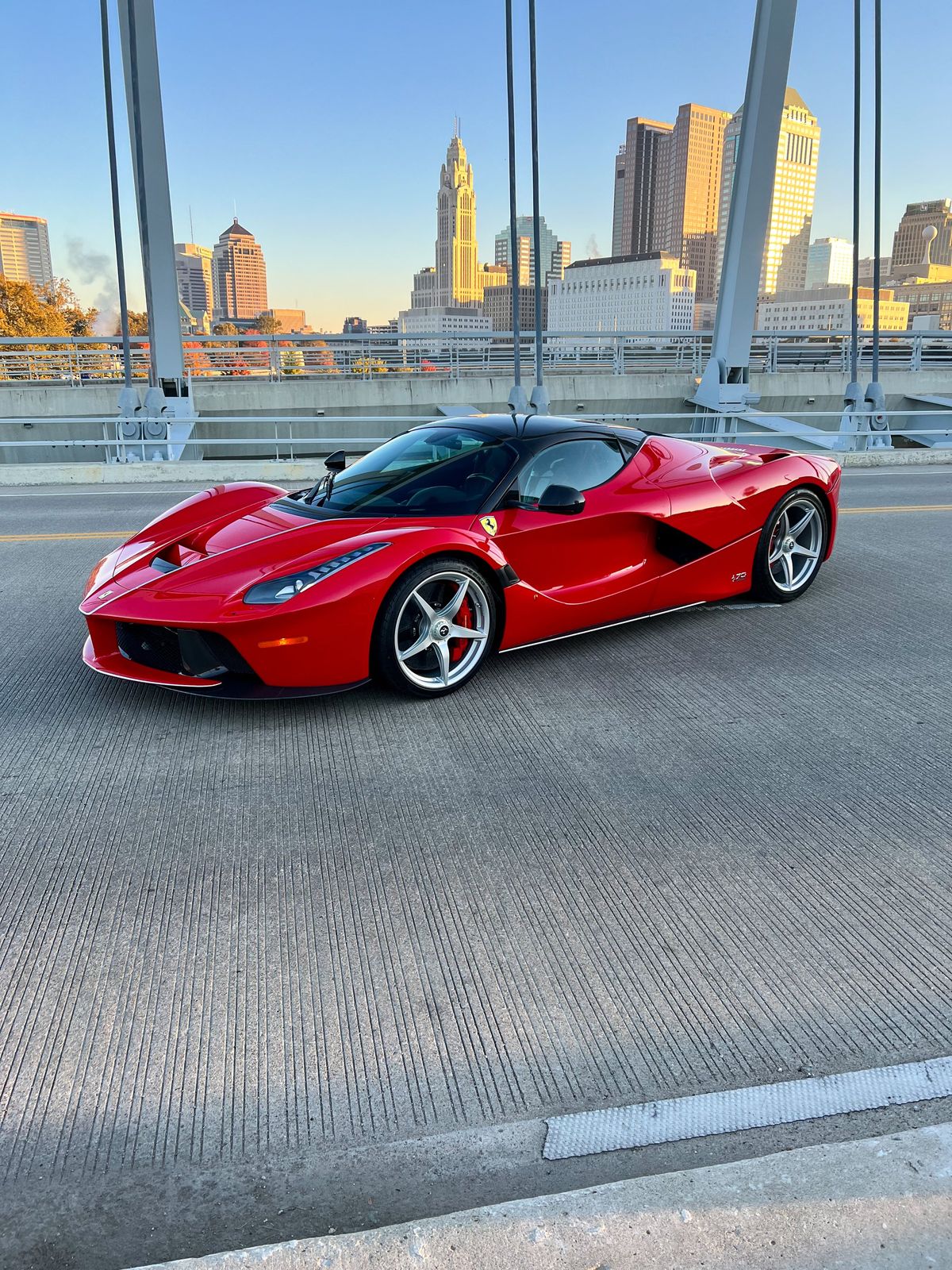 Red Ferrari LaFerrari parked on bridge with city skyline in the background durin