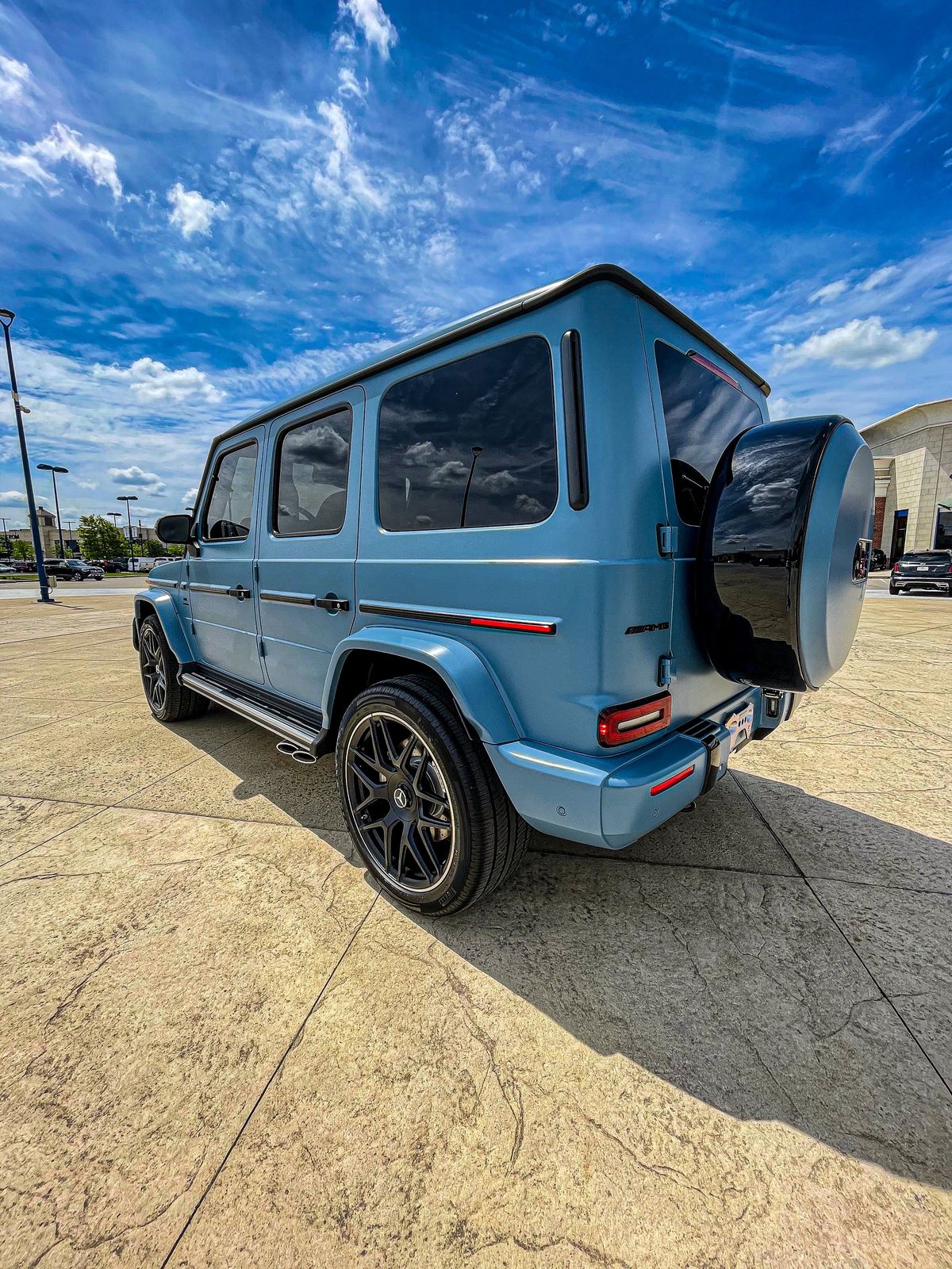 Blue Mercedes-Benz G-Class SUV parked on a paved lot under a partly cloudy sky.