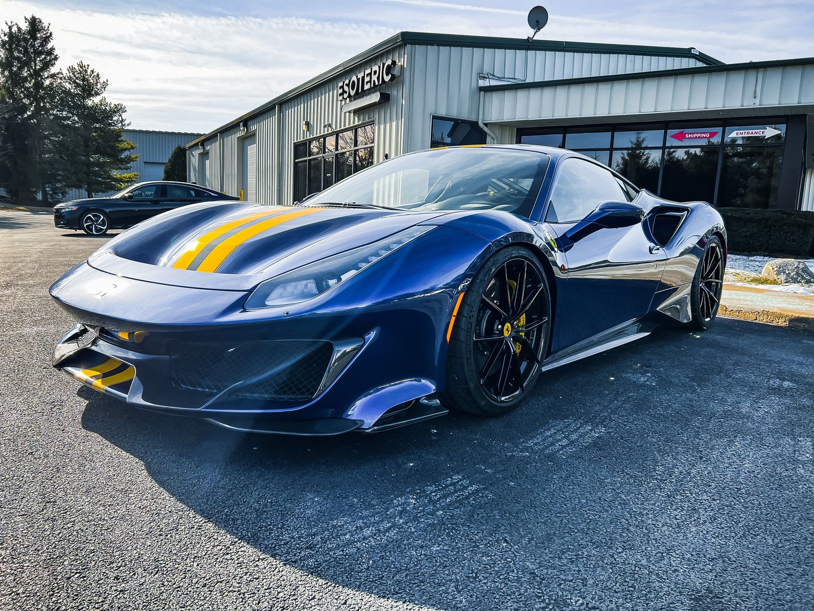 Blue sports car with yellow racing stripes parked in front of a building labeled