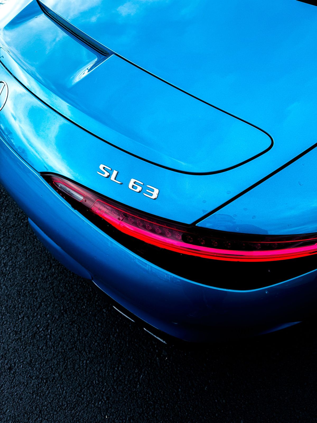 Rear of a blue Mercedes-Benz SL 63 car with a red taillight and chrome badges, o