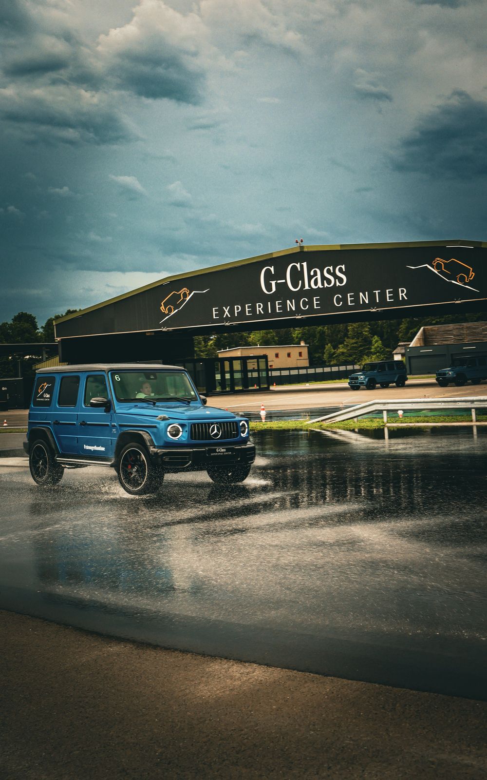 A blue Mercedes-Benz G-Class SUV driving on a wet racetrack during a rainy day a