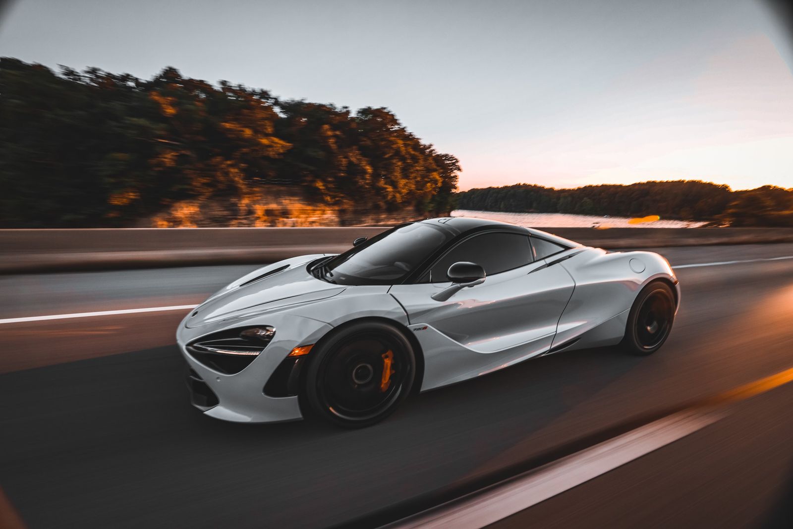 A white sports car driving on a highway during sunset with trees and water in th