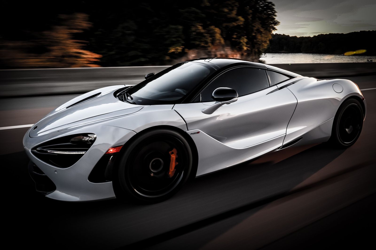 A sleek, silver sports car speeding on a highway at dusk with trees and a body o