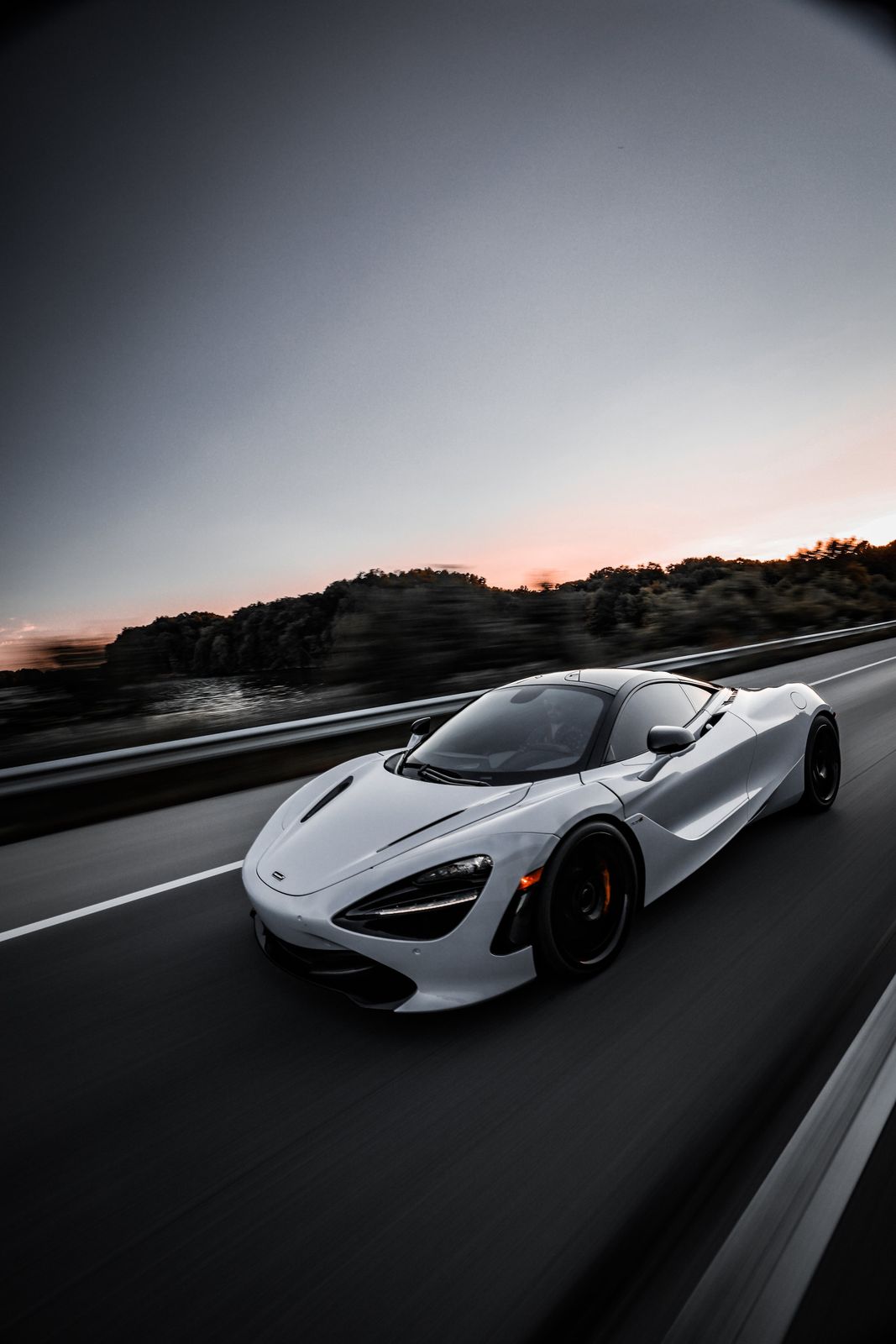 A white sports car on a highway at sunset, with trees and sky in the background.