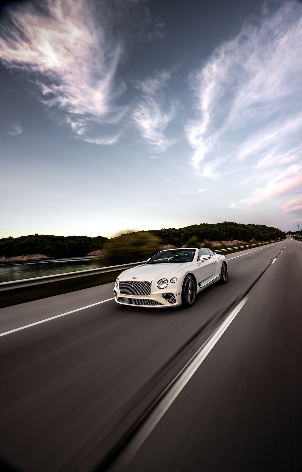 A white luxury convertible car driving on an empty highway with scenic green hil
