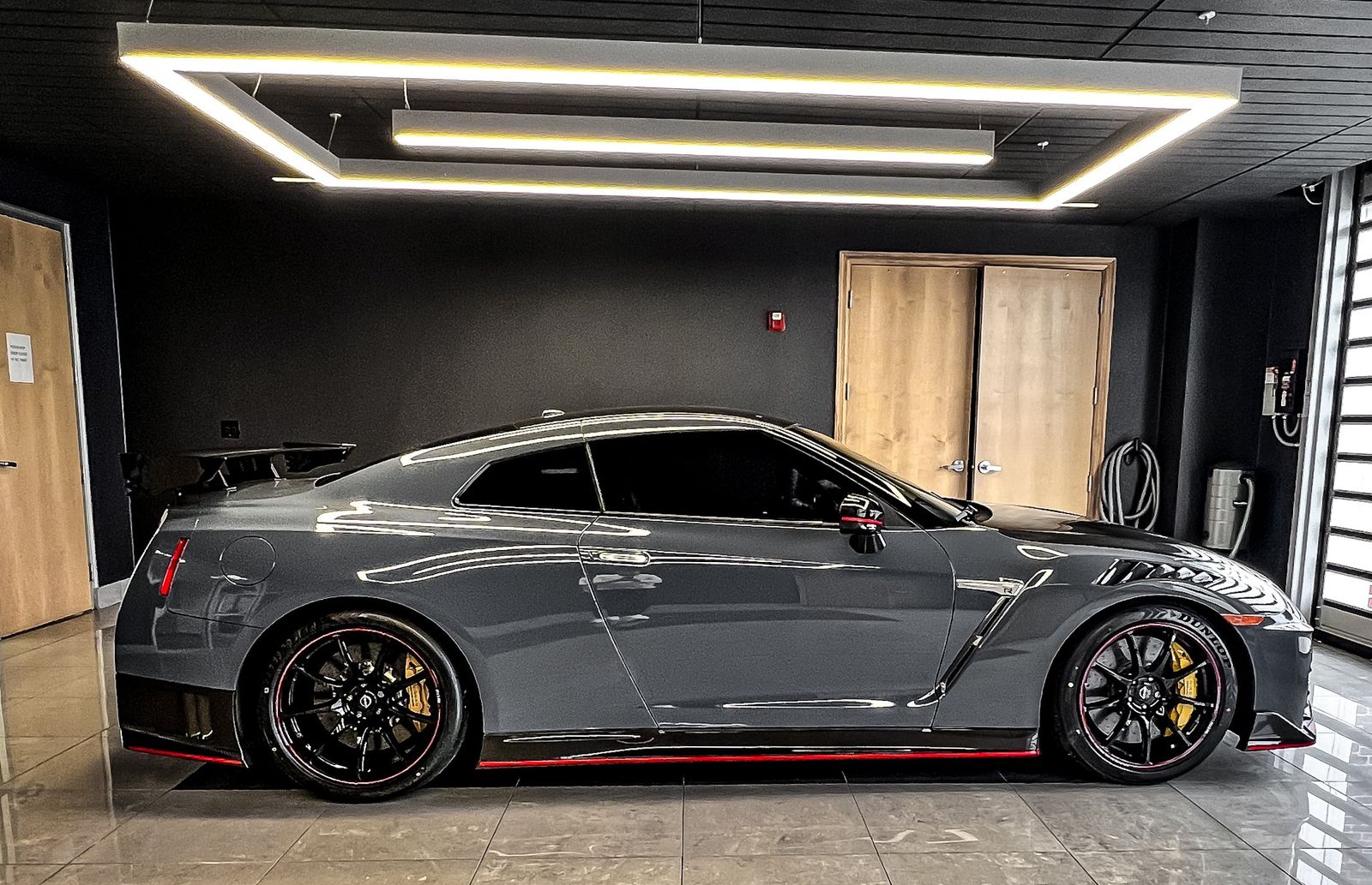 Gray sports car with black rims and yellow brake calipers parked indoors next to