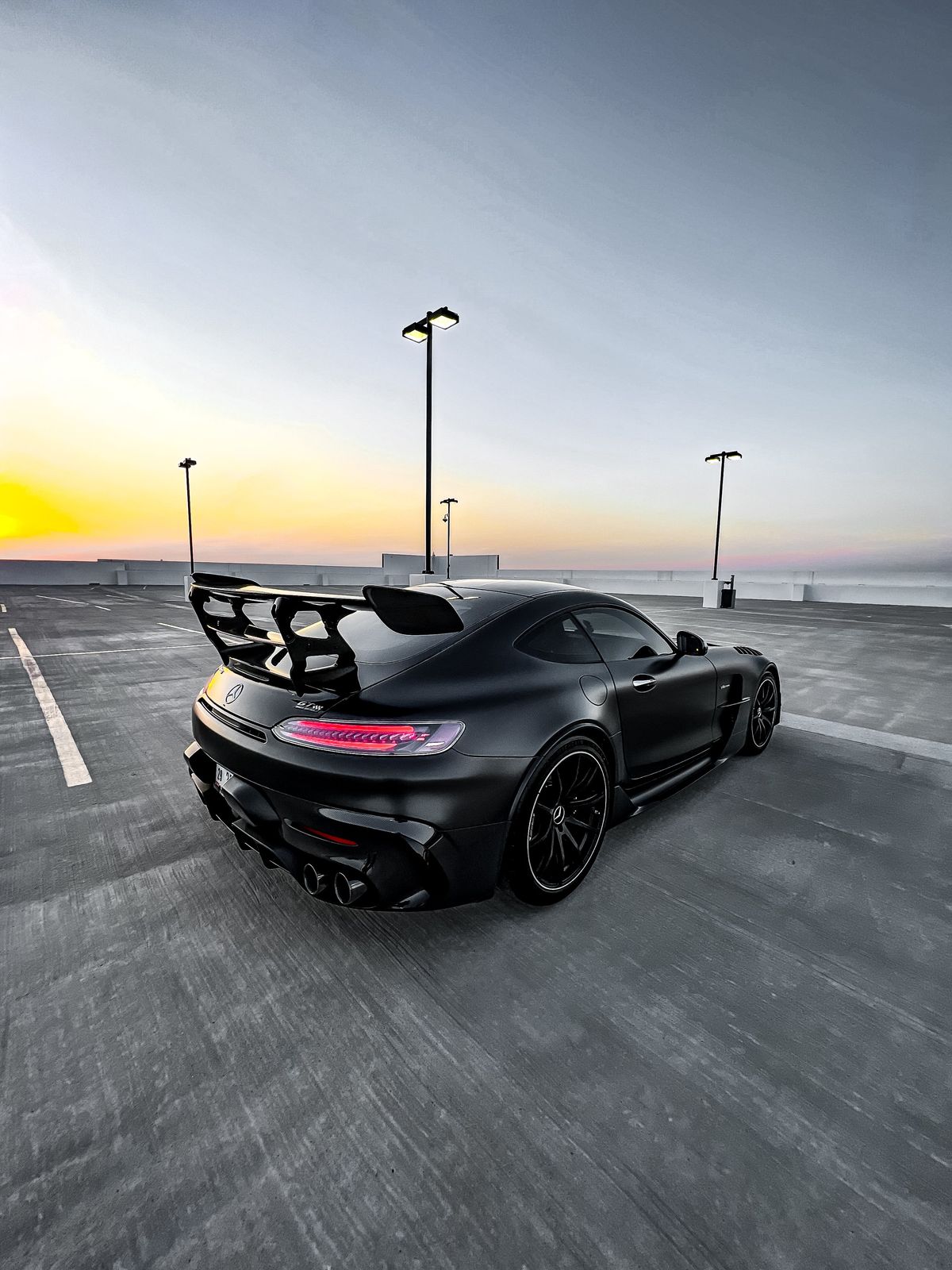 A matte black sports car with a prominent rear spoiler parked in an empty roofto