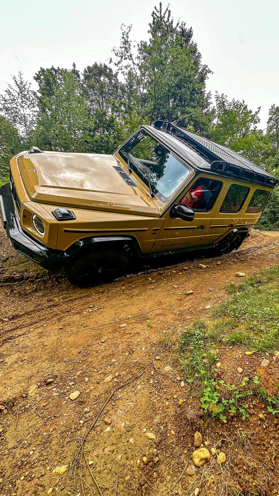 A tan-colored off-road vehicle, partially stuck on a dirt trail, surrounded by g